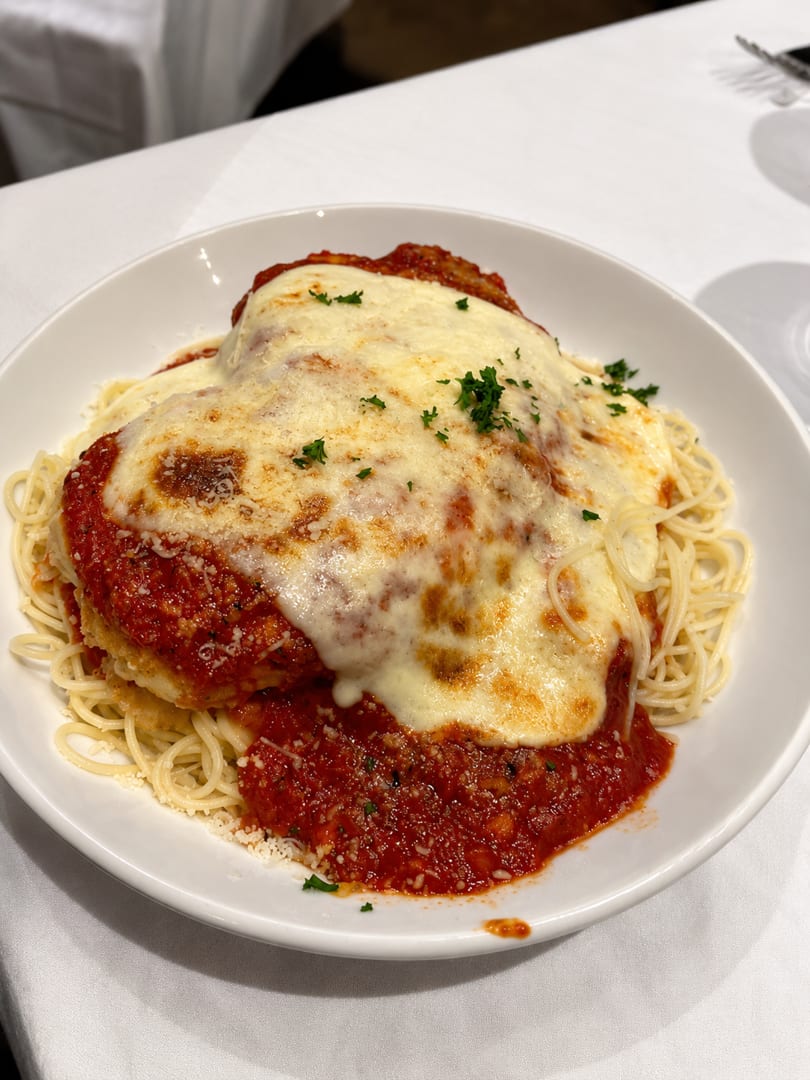 Chicken parmesan with melted cheese and marinara sauce, served over spaghetti on a white plate.