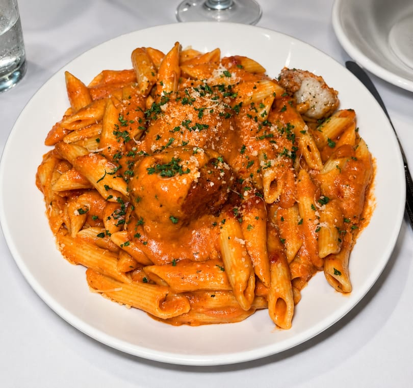 Penne pasta with meatballs in a creamy tomato sauce, topped with parsley and parmesan cheese.