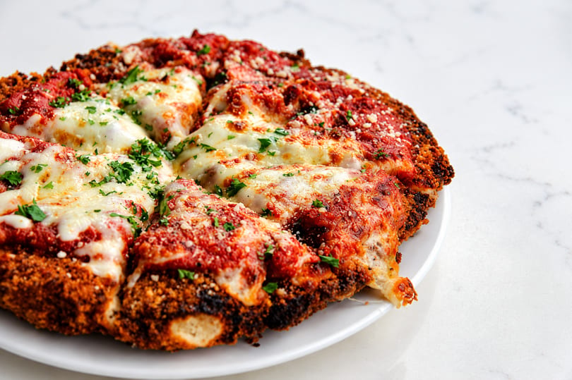 Close-up of a deep-dish pizza with melted mozzarella, red sauce, and parsley on a white plate.